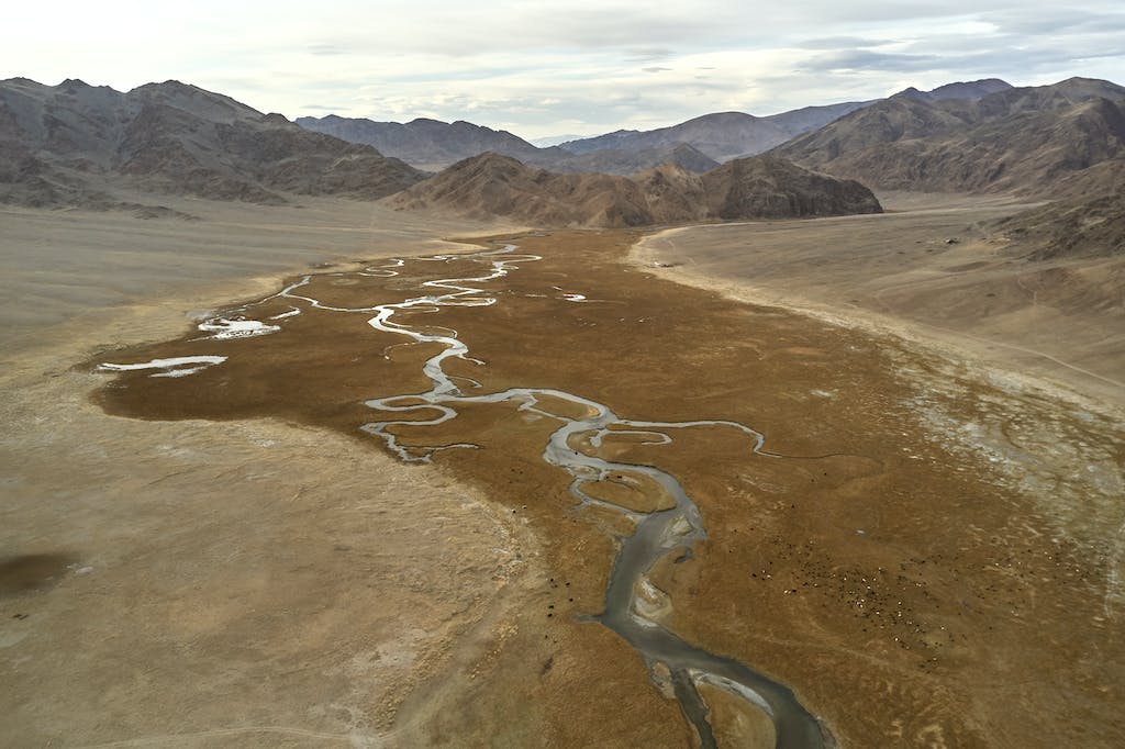 Drone view of narrow riverbeds flowing on rough terrain near mountains in daytime
